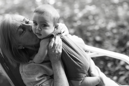Beautiful happy smiling senior elderly woman holding on hands cute little baby boy sitting outdoor....