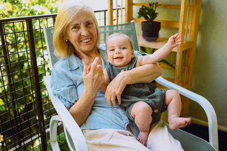 Beautiful happy smiling senior elderly woman holding on hands cute little baby boy sitting on...