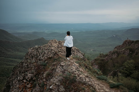 Woman tourist hiking up goes to top of mountain enjoying nature. Landscape in cloudy gloomy windy...