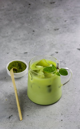 A cup of antioxidant matcha drink made of ground powder of green tea leaves with milk, ice cubes and fresh mint on a serving tray with matcha spoon and matcha powder bowl. Iced matcha latte. Copy space. Iced matcha green teaの写真素材