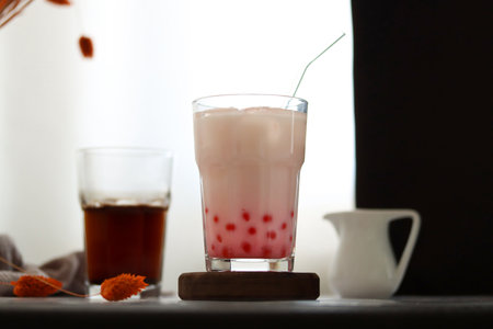 Home made milk bubble tea with tapioca pearls. Iced strawberry milk tea drink with tapioca balls. Milky drink with tapioka bubbles and ice. Bubble tea or boba tea on a table, home interiorの写真素材