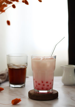 Home made milk bubble tea with tapioca pearls. Strawberry iced milk tea drink with tapioca balls. Milky drink with tapioka bubbles and ice. Bubble tea or boba tea on a table, home interiorの写真素材