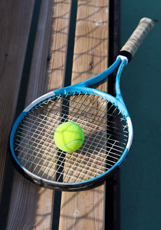 Tennis racket and ball on a bench at the blue hard tennis court. Hard lighting. Summer sport concept. Active lifestyle and healthy living, close upの写真素材