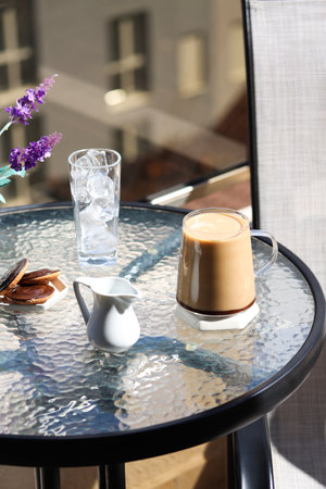 A cup of coffee with milk or hot chocolate with cookies and a glass of ice on a table on a terrace in a cafe on a high floor, blurred city view. Having breakfast with coffee on a terraceの写真素材