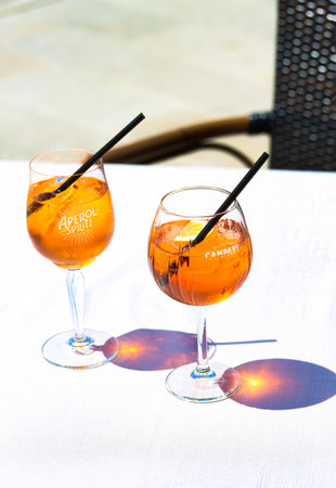 Aperol Spritz and Campari Orange cocktails with orange slices and ice in wine glasses on a restaurant table at the sea coast on a sunny day. Holiday concept. Set of summer drinks, live photoの写真素材