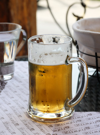 Frosty mug of cold light beer on the table in a restaurant or in a bar. Mug of cold beer, refreshing summer drink. Holiday concept. Live photo of having a glass of beer for lunch in vacationの写真素材