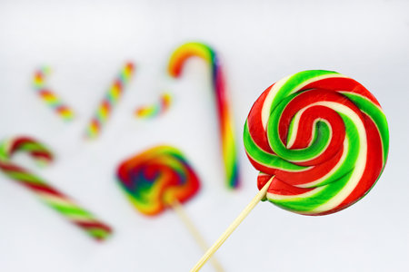 Colorful round lollipop, bright sweet candy in white, red and green colors. Christmas or New year lollipop on white background with other multicolored lollipops blurred behind. Close upの写真素材