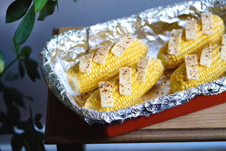 Raw corn on cobs with butter slices and spices in a baking dish. Preparing corn for cooking. vegetable season. Fresh corn cobs ready to cook baked corn with butter, salt and chili flakes. Vegan foodの写真素材