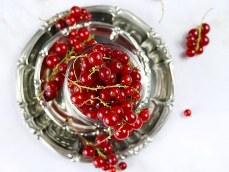 Red currant berries in metallic plate on marble table, close up, top view. Fresh red currants on light background, copy space. Atmospheric photo of ripe red currants in rustic style. selective focusの写真素材