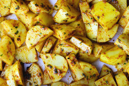 Raw potato slices in spices top view. Fresh potato wedges mixed with herbs and spices in a rustic way ready to be baked or roasted. Raw potatoes with spices on a baking sheet ready to be cookedの写真素材
