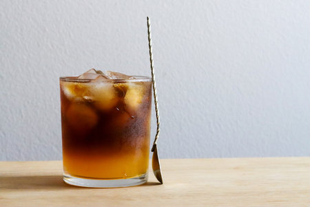 Glass of bumble coffee and barista spoon on wooden table over concrete wall, minimalistic design, copy space. Iced coffee made of orange juice, espresso, caramel syrup and ice cubes. coffee shop menuの写真素材