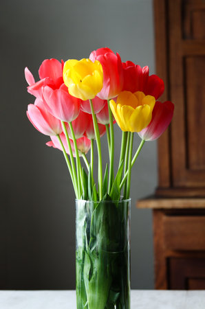 Colorful tulips in a vase with a wooden background. Mother's day or women's day background. Bright tulips in a vase. Elegant bouquet of red and yellow tulips. Mix of pink and yellow tulipsの写真素材