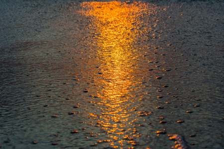 textured background - close up of ocean water on the sand reflecting the orange light of sunriseの写真素材