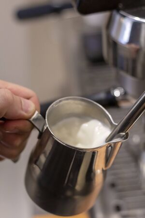 Male bartender on the workplace. Closeup image of male hands pouring milk for coffee in special jugの写真素材