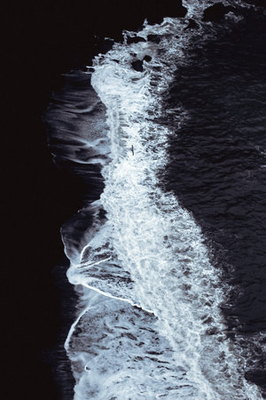 White foam on a black lava beach in southern Iceland. Sea aerial view and top view. Amazing nature,...