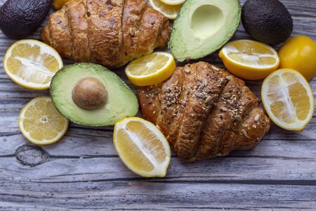composition with fresh baked croissants and fruits, avocado and lemon, on grey wooden backgroundの写真素材
