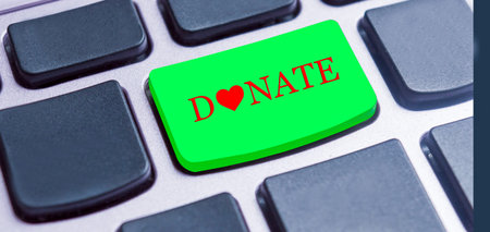 Closeup of a green button with the red letters of  word Donate, on a black keyboard.