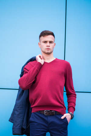 A young guy in a red jacket is holding a jacket on a blue backgroundの写真素材