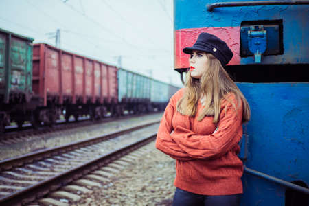 a fashionable girl in a cap standing on the background of a diesel locomotive and a passing freight trainのeditorial素材
