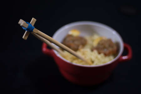 noodles with meatballs in a red bowl and bamboo sticks on a black backgroundの写真素材