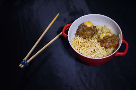 noodles with meatballs in a red bowl and bamboo sticks on a black backgroundの写真素材