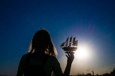 Silhouette of a girl at sunset holding a shipの写真素材