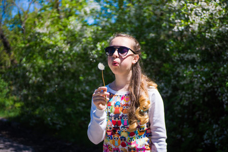 A teenage girl blowing a dandelion in a sunny bright day in an outdoor park