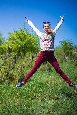 A teenage girl in a park jumps in the air on a sunny and bright day