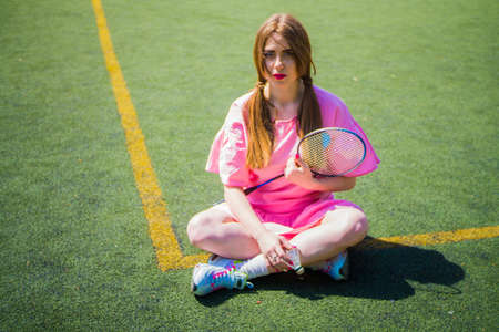 A girl sits on a football field on a sunny and bright day doing sports and playing a game of badmintonの写真素材
