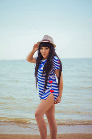 Brunette girl in hat and striped dress on the seashoreの写真素材
