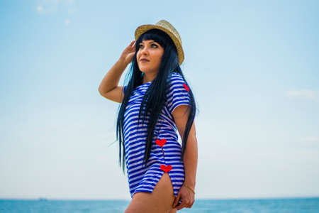 Brunette girl in hat and striped dress on the seashoreの写真素材