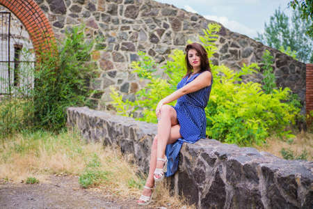 The brunette girl in a blue long dress against the background of a fenceの写真素材