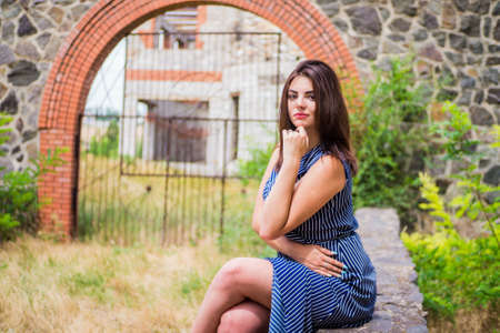 The brunette girl in a blue long dress against the background of a fenceの写真素材