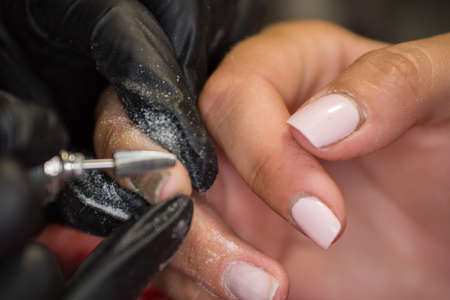 The master of nail extensions and coating with gel varnish makes correction to his client in the beauty salonの写真素材