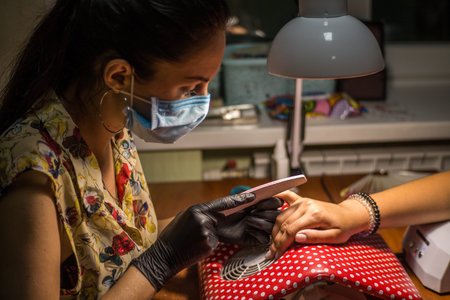 The master of nail extensions and coating with gel varnish makes correction to his client in the beauty salonの写真素材