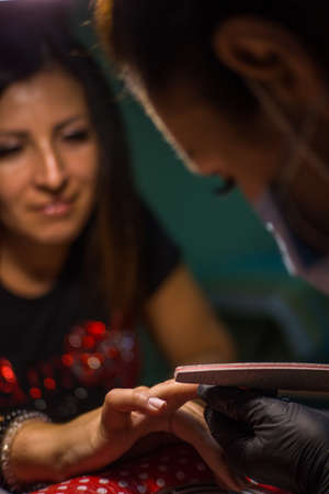 The master of nail extensions and coating with gel varnish makes correction to his client in the beauty salonの写真素材