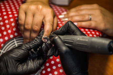 The master of nail extensions and coating with gel varnish makes correction to his client in the beauty salonの写真素材