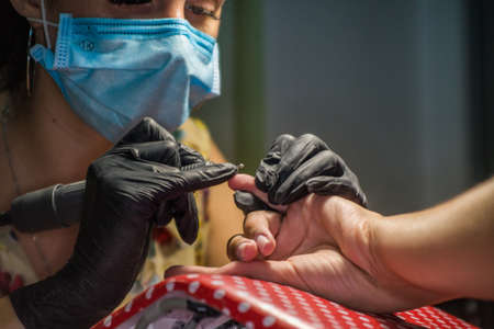 The master of nail extensions and coating with gel varnish makes correction to his client in the beauty salonの写真素材