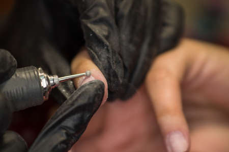 The master of nail extensions and coating with gel varnish makes correction to his client in the beauty salonの写真素材