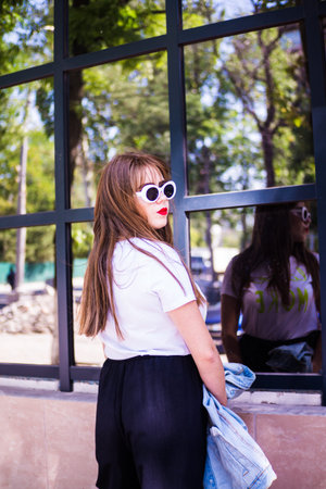 A fashionable and stylish girl in wide black pants, a white T-shirt with sunglasses with a white rim...