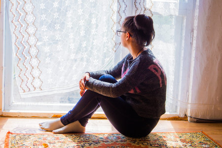 A brunette girl with a tail on her head and glasses for a sight, sits on the floor near a large...