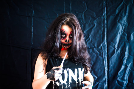 Dead girl brunette with a makeup skeleton is awesome with a game of knife on a black background, a...