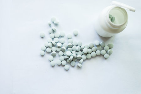 White jar with vitamins A, B, C scattered on a white background