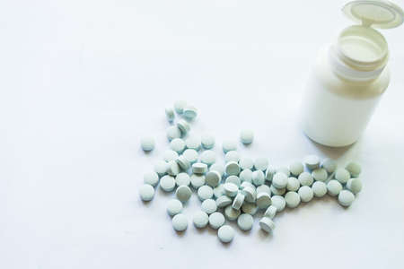 White jar with vitamins A, B, C scattered on a white backgroundの写真素材