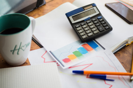 On the home table are stock and finance charts with a calculator, a coffee mug, a pencil, a marker...