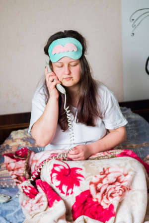 A young girl woke up early in the morning from a phone call, with a blindfold on her eyes, at home in bed in her room.の写真素材