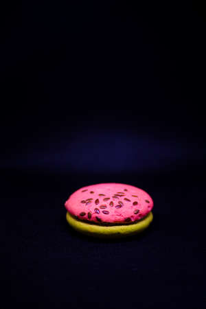 Multi-colored green and pink, bright cookies with two halves seasoned with filling and sprinkled with sesame seeds on a bright black color background.の写真素材
