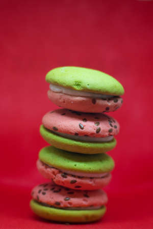 Multi-colored green and pink, bright cookies with two halves dressed with filling and sprinkled with sesame seeds on a bright red color background.の写真素材