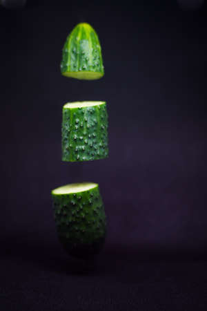 Close-up of a cucumber cut into three parts in the air on a black background.の写真素材