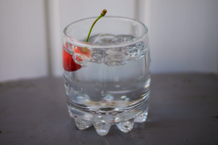 Ripe cherries in a glass with water on a table with a textured wooden wall